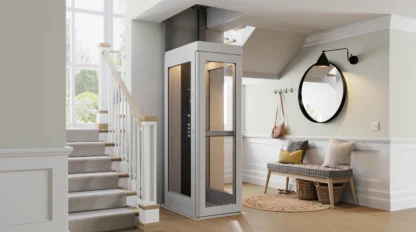 A modern residential elevator is installed next to a staircase in a bright, contemporary entryway with a bench, mirror, and coat hooks.