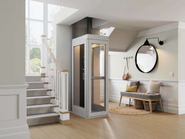 A modern residential elevator is installed next to a staircase in a bright, contemporary entryway with a bench, mirror, and coat hooks.