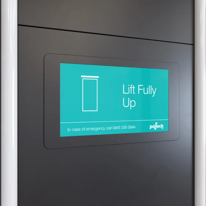 Auf einem digitalen Display an der Wand ist ein Aufzugssymbol mit dem Text „Aufzug vollständig oben“ zu sehen, darunter eine Notrufnummer.
