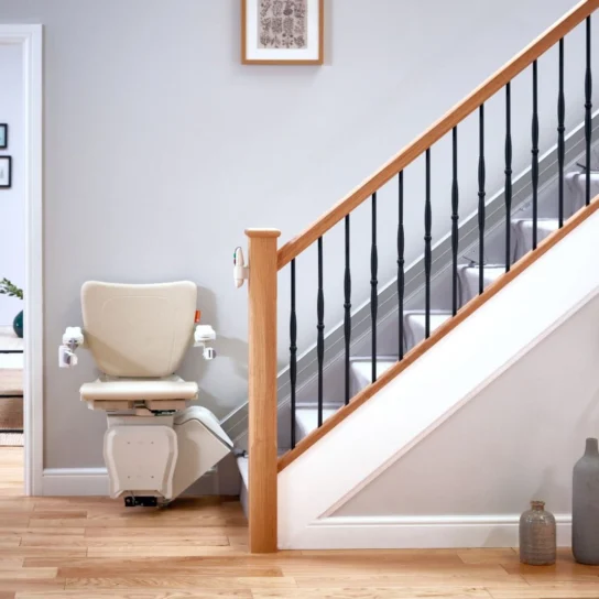 A modern stairlift is installed along a staircase in a bright, tidy home interior with wooden floors and minimalist decor.