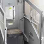 A stairlift chair with armrests, a small control panel, and safety railings installed beside a staircase, with a mirror mounted on the wall.