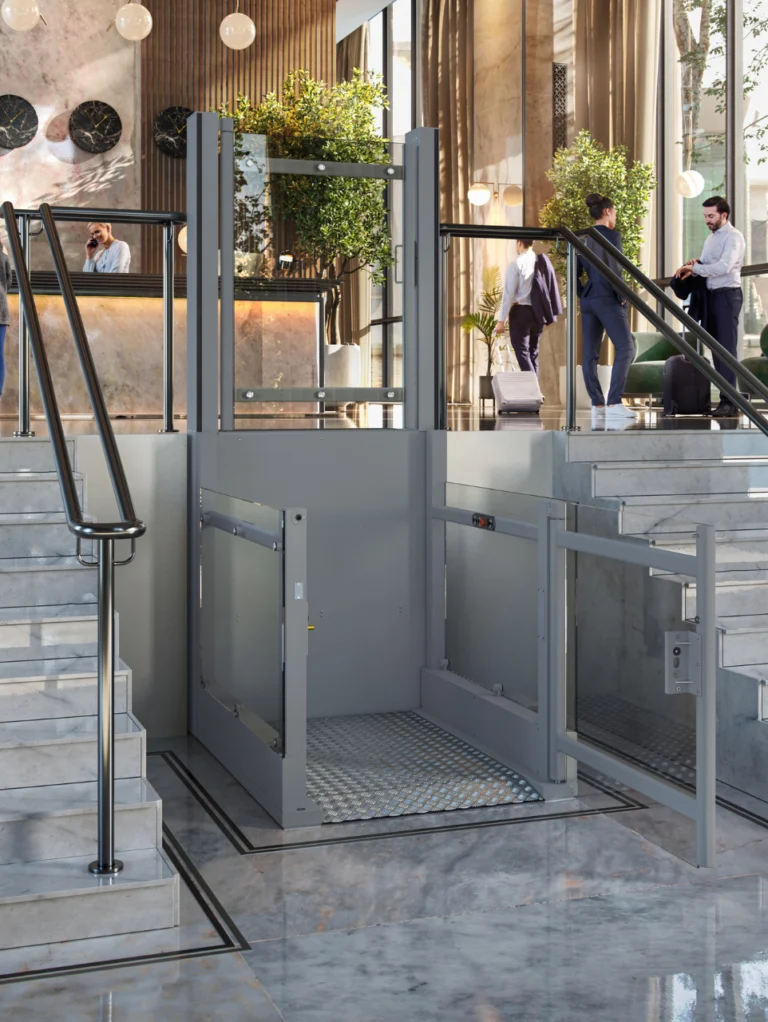A modern hotel lobby features a platform lift for accessibility between marble staircases, with people interacting in the background near the reception desk.