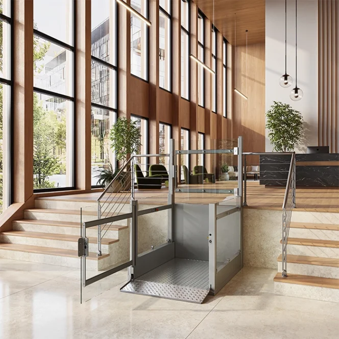 A platform lift is installed between two sets of stairs in a modern, spacious lobby with large windows, plants, and hanging lights.