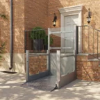A metal wheelchair lift installed outside a brick building provides accessible entry to a raised doorway with stairs and black railings.