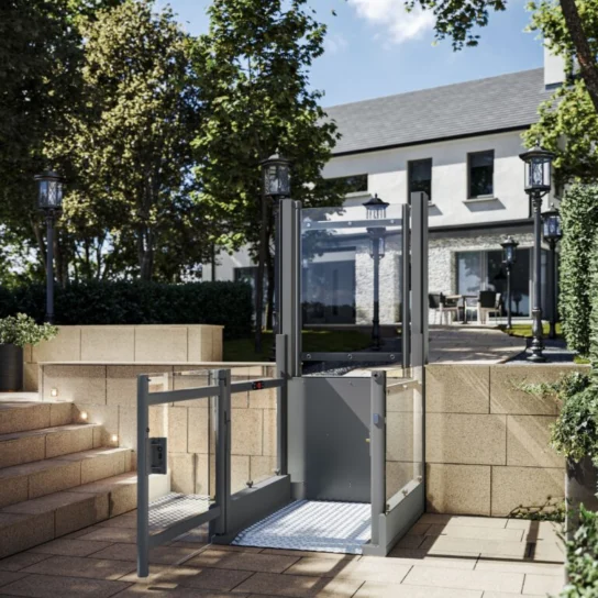 A modern outdoor wheelchair lift is installed beside stone steps, providing accessible entry to a patio area near a contemporary house.