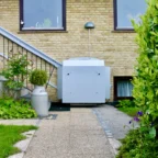 A white wheelchair lift is installed next to stairs outside a brick house, providing accessible entry from a garden pathway.