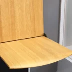 A wooden folding chair attached to a wall, shown in an open position against a gray and white background.