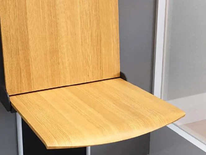 A wooden folding chair attached to a wall, shown in an open position against a gray and white background.