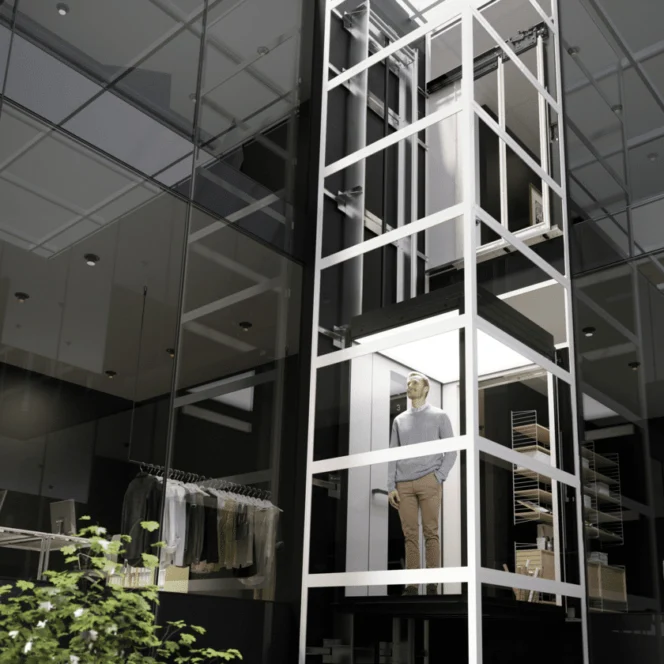 A man stands inside a modern glass elevator within a contemporary building featuring office and closet spaces.