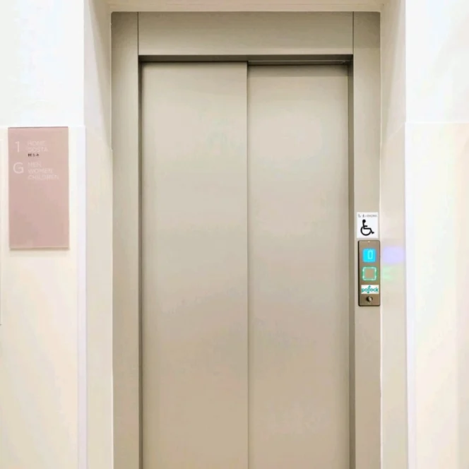 A closed silver elevator door beneath a sign that reads "LIFT" in uppercase letters, with control buttons on the right side, including an accessibility symbol.