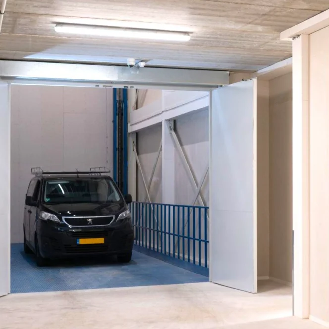 A black van with a yellow license plate is parked inside a modern indoor parking lift with open white doors and concrete ceiling.