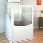 A small residential home elevator with transparent panels installed in a living room with wooden flooring and modern decor.