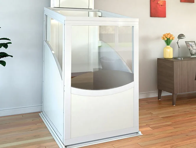 A small residential home elevator with transparent panels installed in a living room with wooden flooring and modern decor.