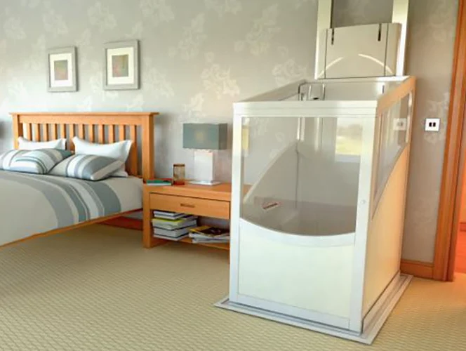 A compact home elevator is installed next to a wooden bed in a tidy bedroom with beige carpeting and light-colored walls.